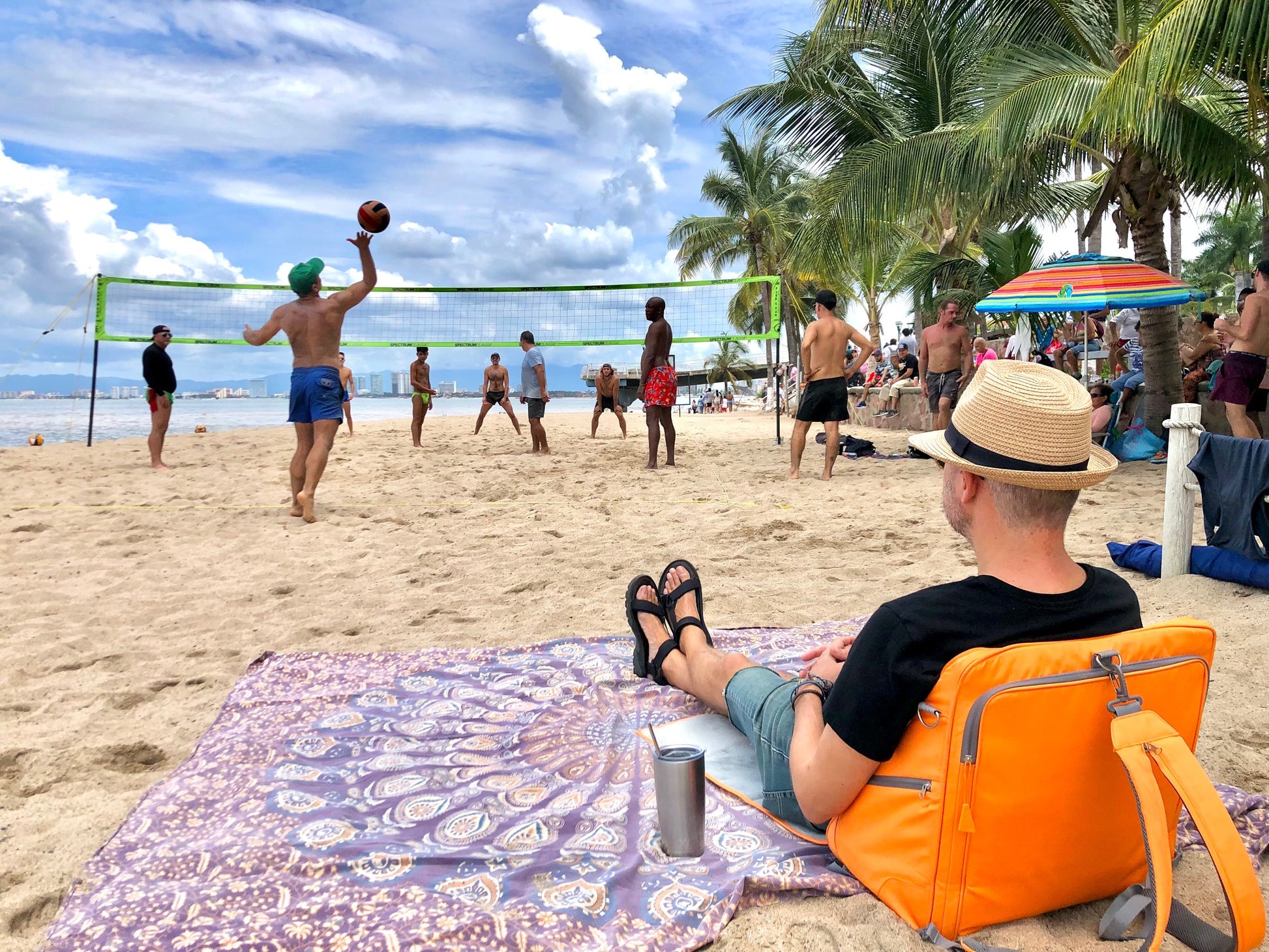 A man with a hat observes a sand volleyball game while using his Playamigo beach chair.